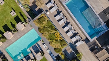 Vista aérea de un complejo turístico con una amplia piscina, tumbonas y una zona de terraza de madera.