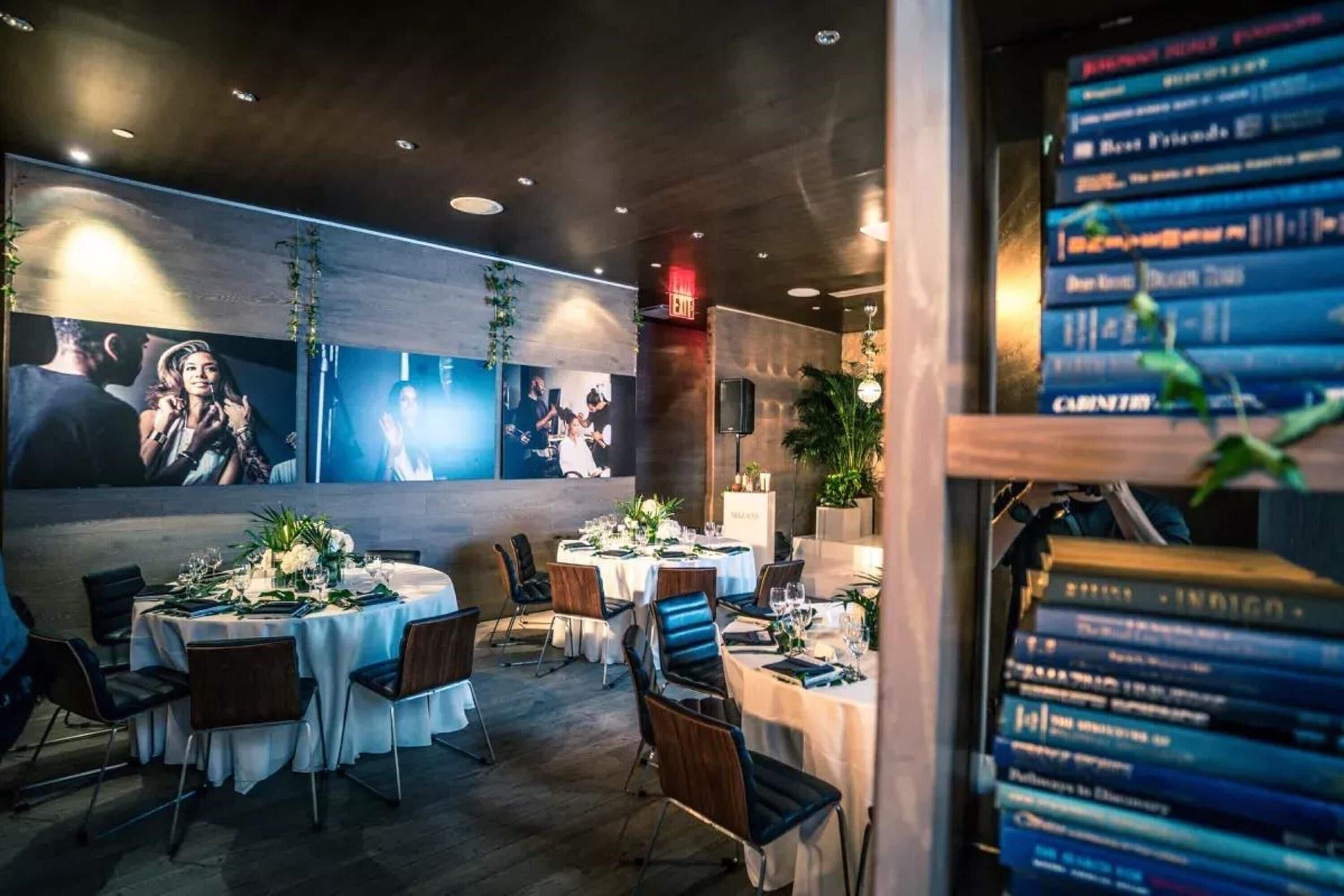 A restaurant with round tables set for dining, a bookshelf with books, and a wall with framed pictures.
