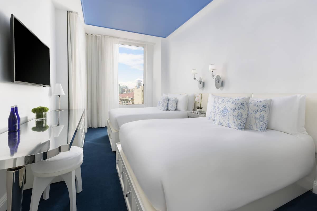 Une chambre d’hôtel avec deux lits, un bureau, une chaise, une télévision et une fenêtre donnant sur la ville.