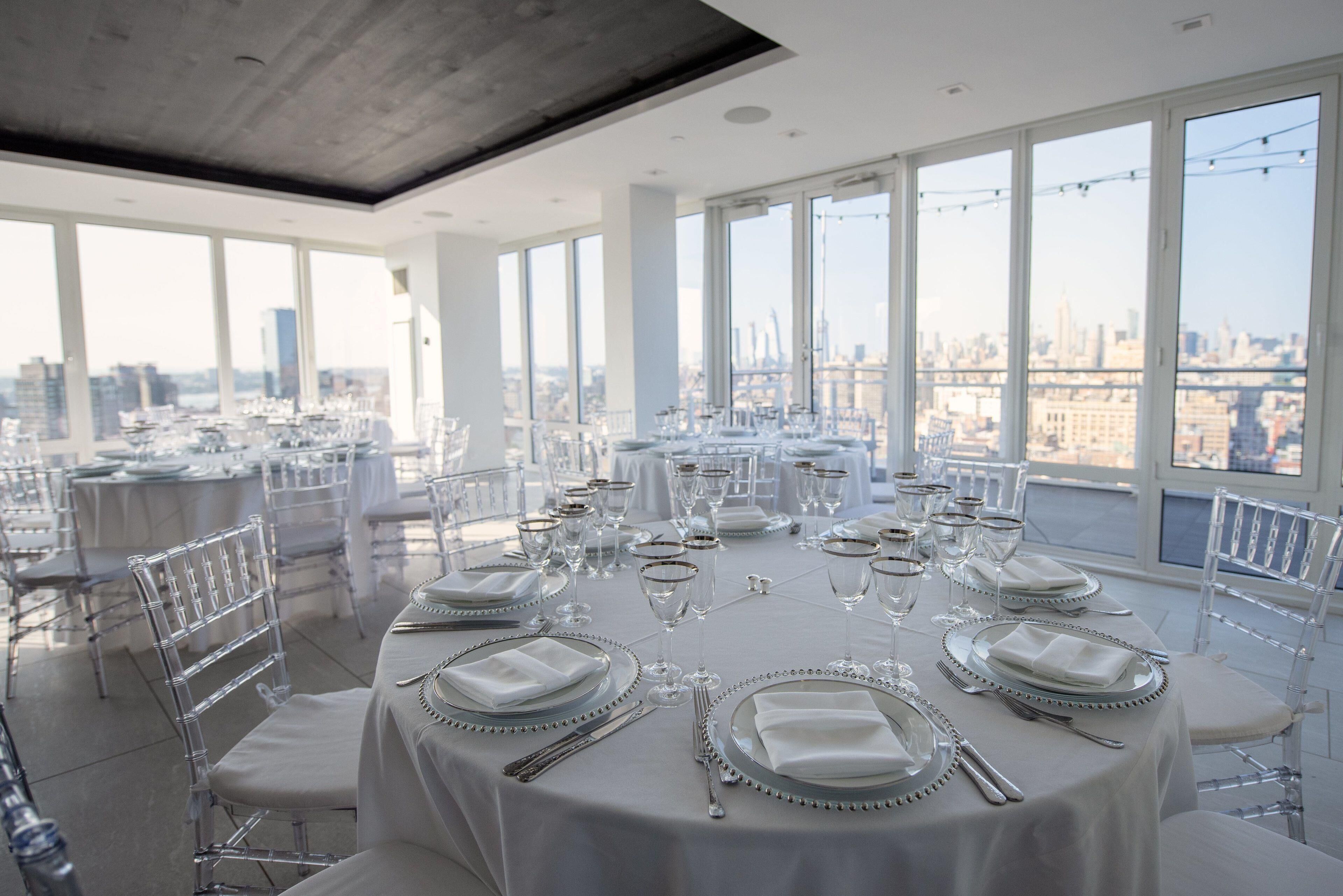 A high-rise dining area with round tables set for a formal event, large windows offering a city view.