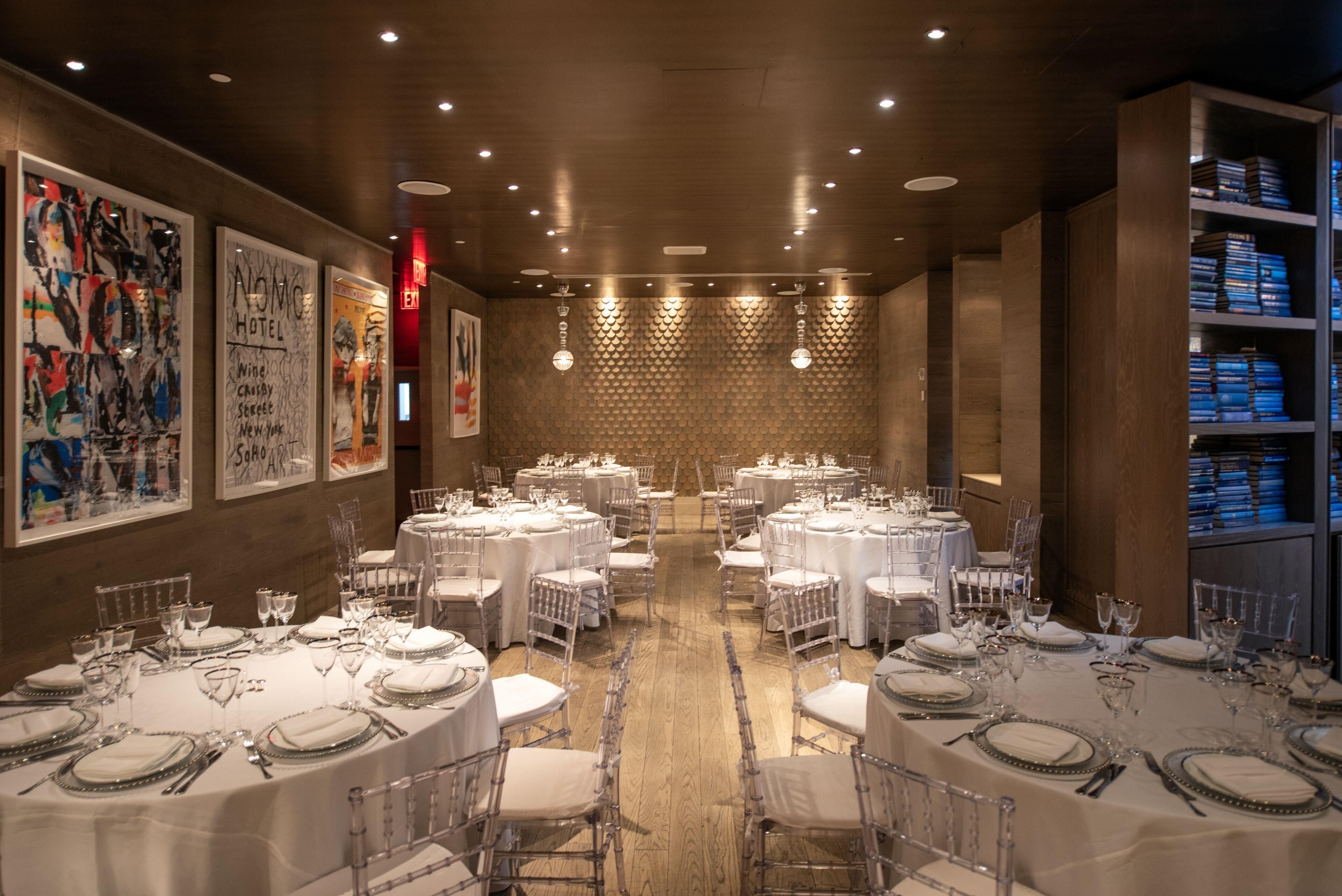A spacious dining area with round tables set for multiple guests, featuring clear chairs and white tablecloths.