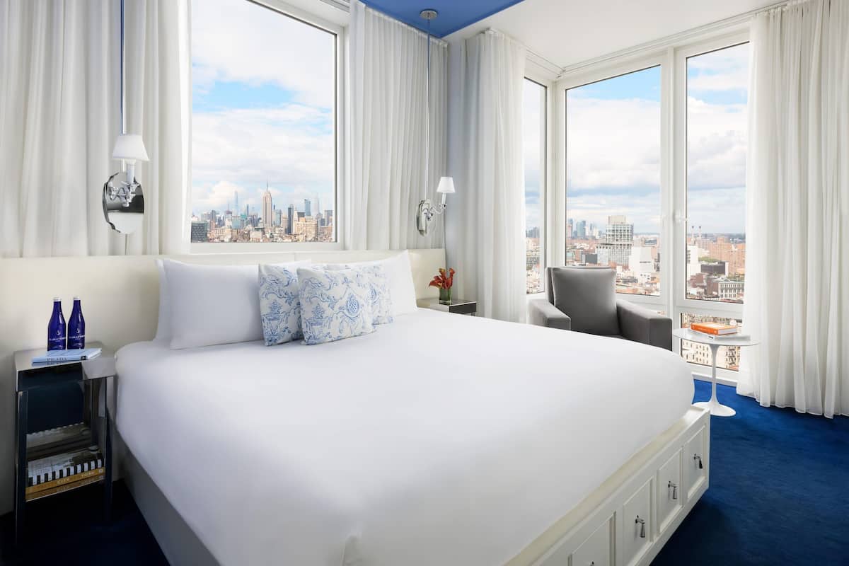Une chambre d’hôtel avec un grand lit, une vue sur la ville, une petite table et une chaise.