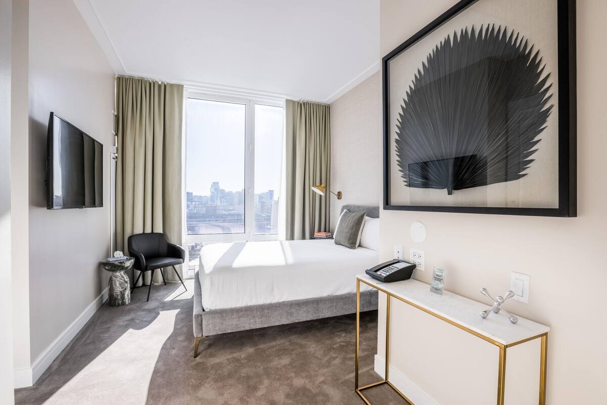 Une chambre d’hôtel moderne dotée d’un grand lit, d’un bureau, d’une chaise, d’une télévision et offrant une vue sur la ville.