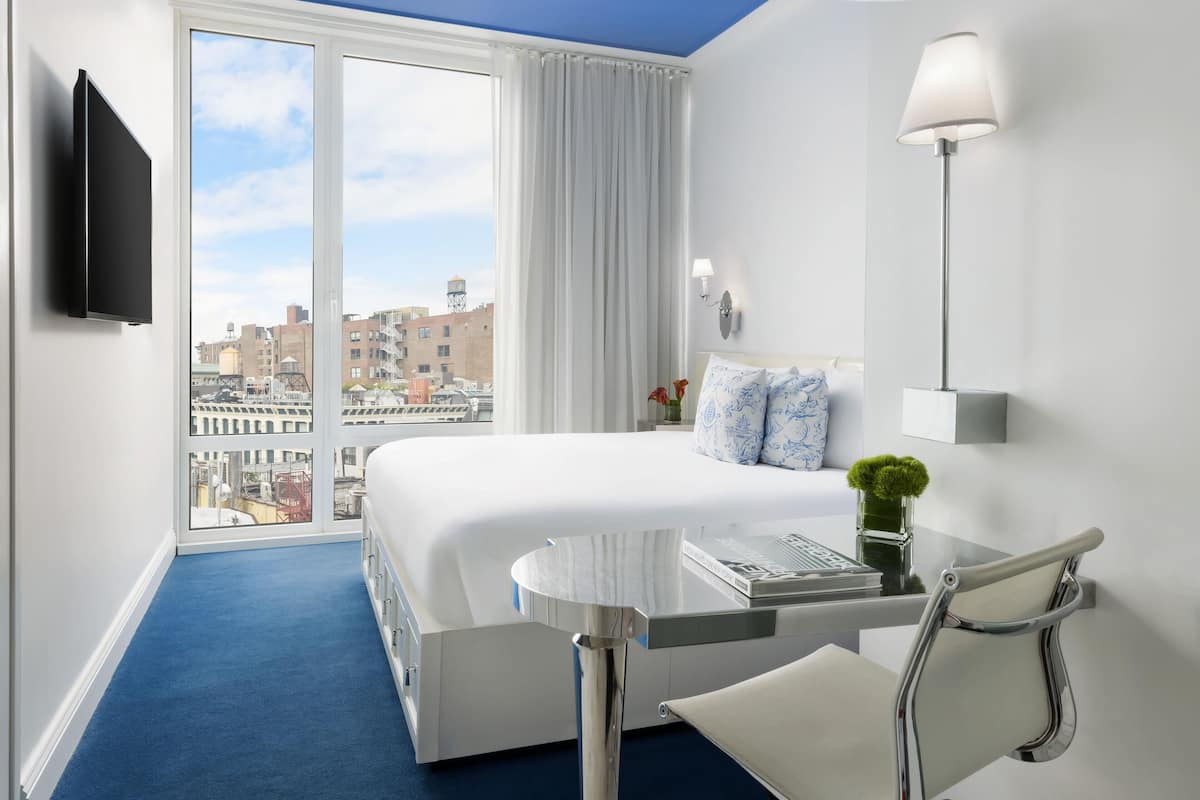Une chambre d’hôtel avec un grand lit, un bureau, une chaise, une télévision et une vue sur la ville.