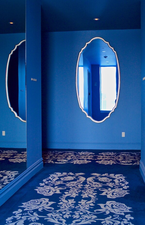 A hallway with blue walls, a large mirror, and a patterned carpet.