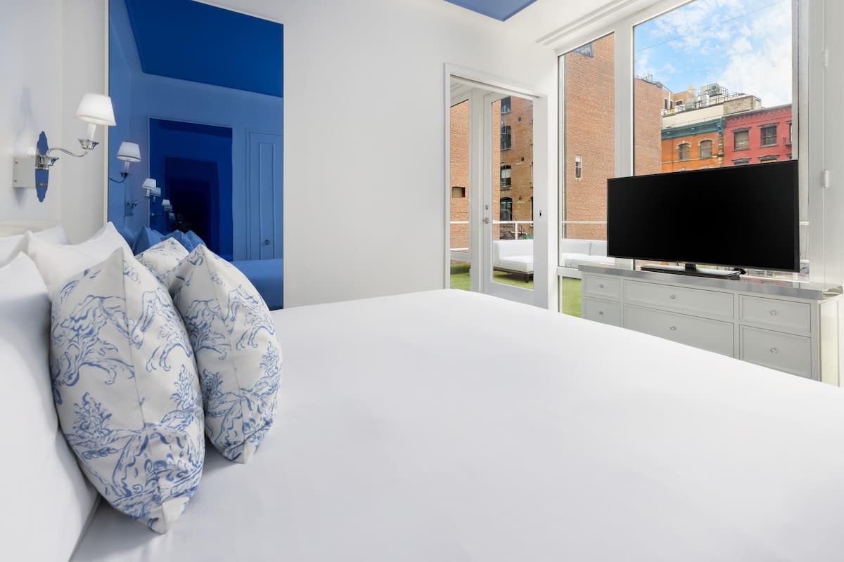 Une chambre dotée d’un grand lit, d’un téléviseur à écran plat et offrant une vue sur les bâtiments par la fenêtre.