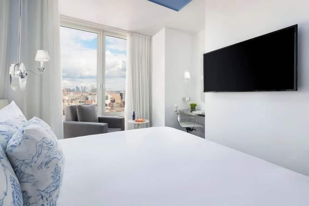 Une chambre d’hôtel avec un grand lit, un bureau, une chaise, une télévision et une vue sur le paysage urbain.