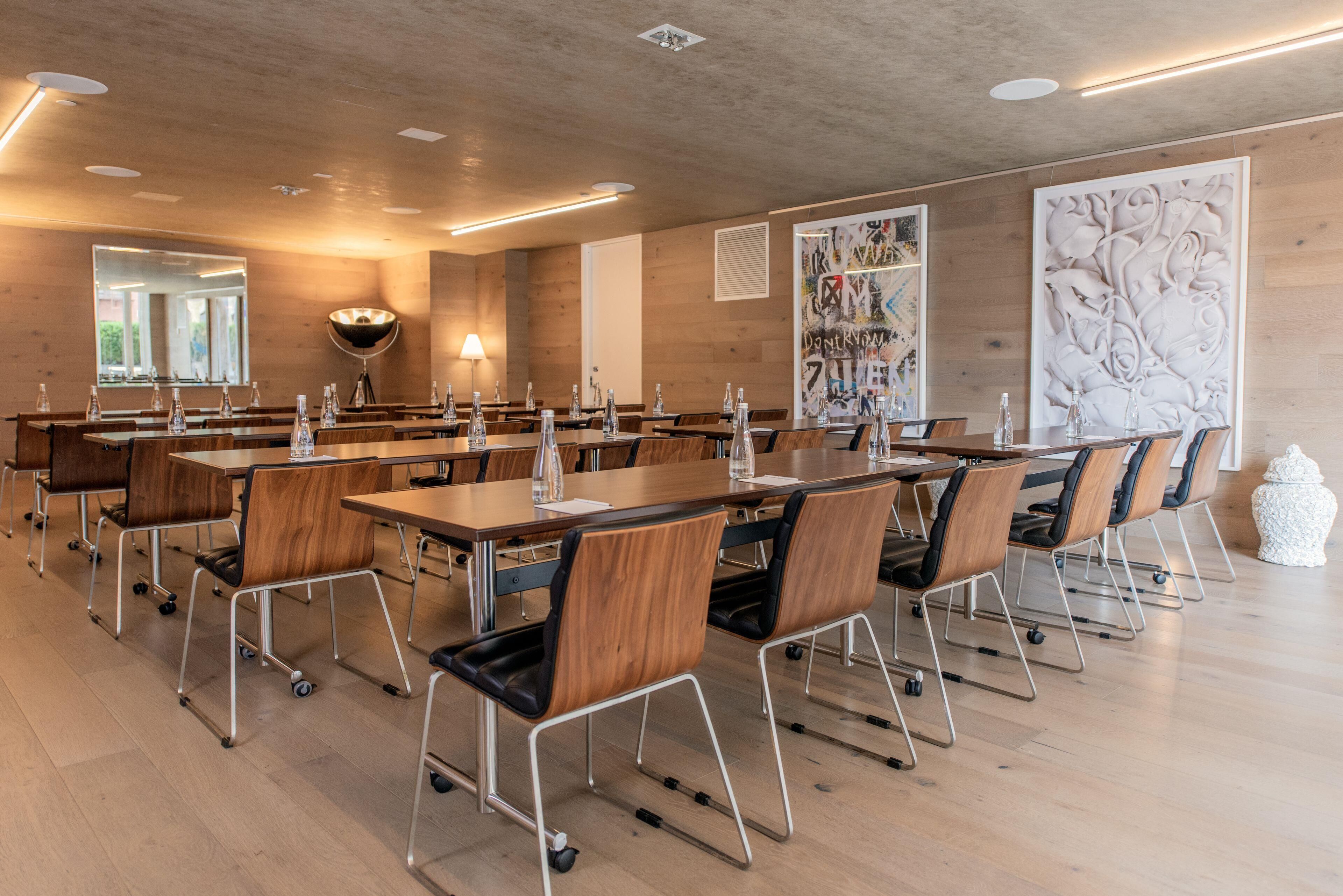 Un salón de conferencias con mesas y sillas de madera, un espejo grande y obras de arte en las paredes.
