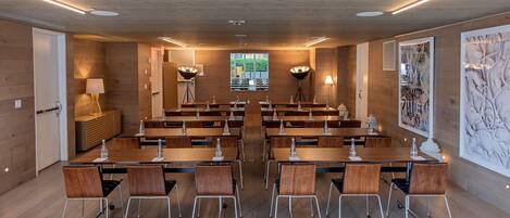 A conference room with wooden tables and chairs, a large window, and modern lighting fixtures.