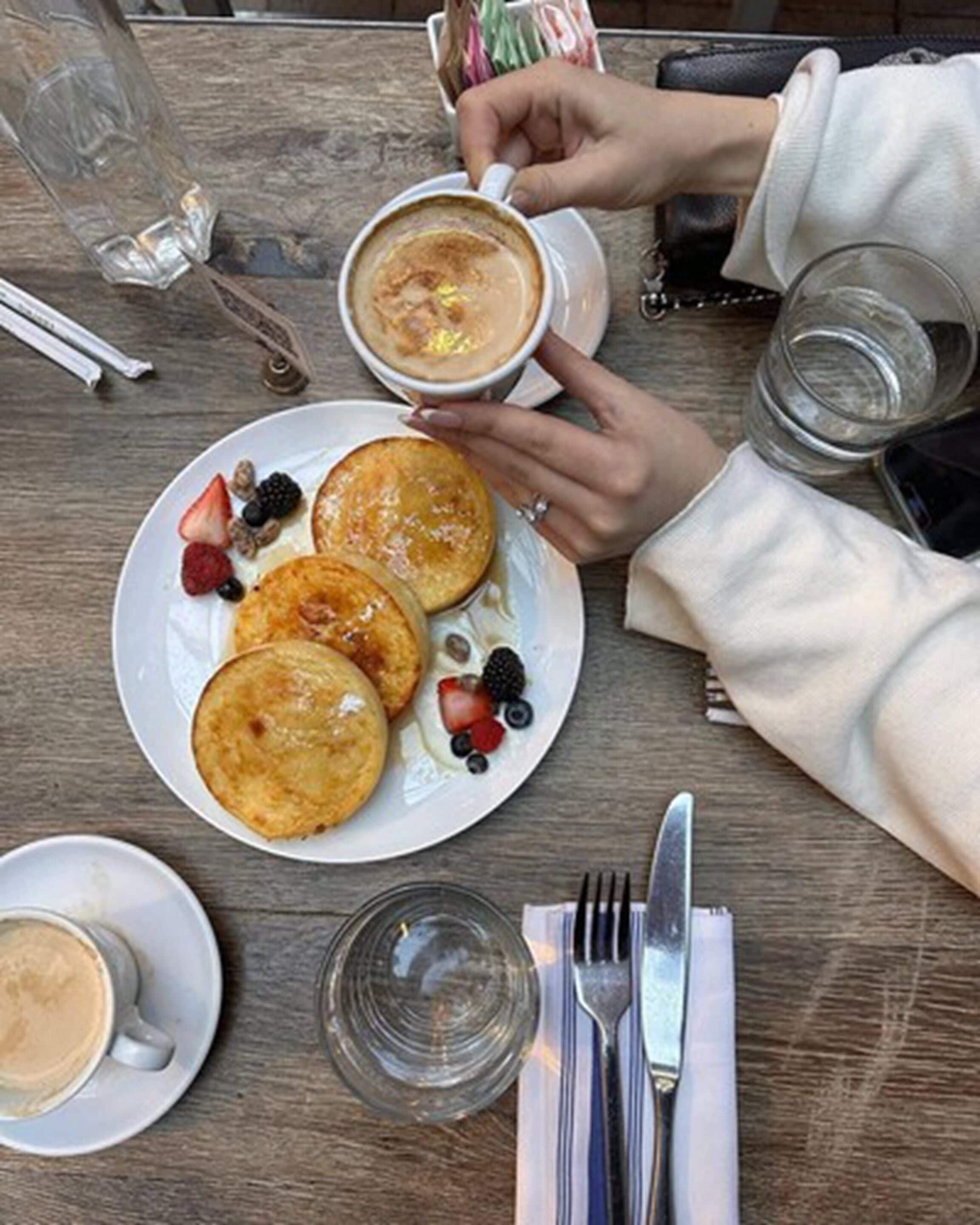 En frukostuppdukning med pannkakor, bär och en kopp kaffe på ett träbord.
