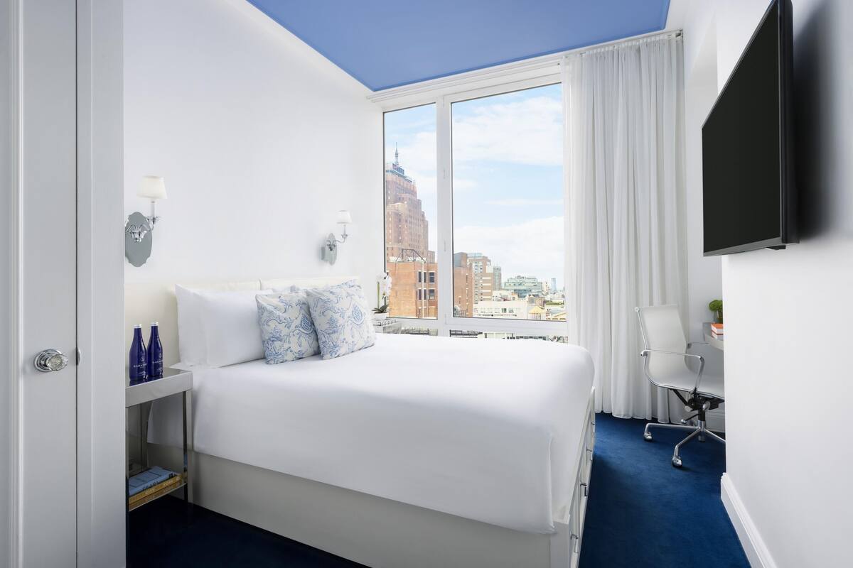 Une chambre d’hôtel avec un grand lit, un bureau, une chaise, une télévision et une fenêtre donnant sur la ville.