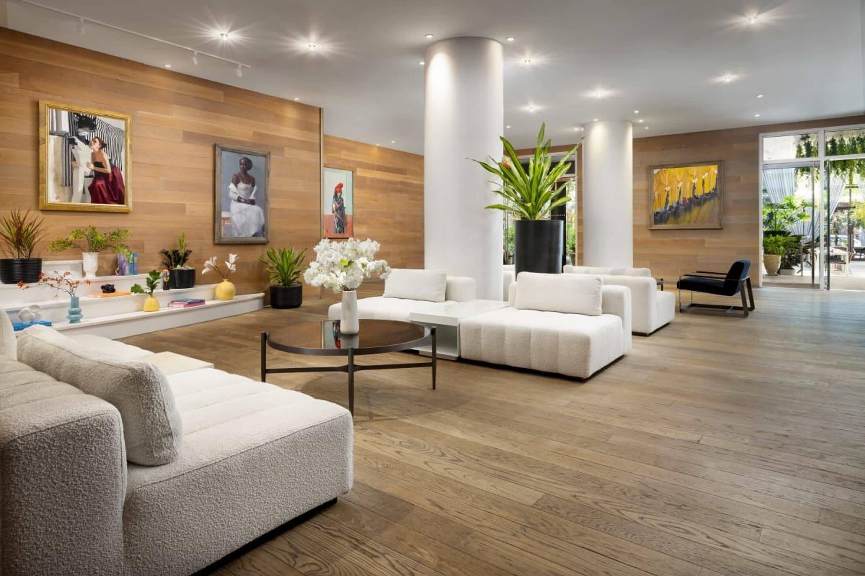 A spacious lobby with a modern design, featuring a white sofa set, a coffee table, and several potted plants.