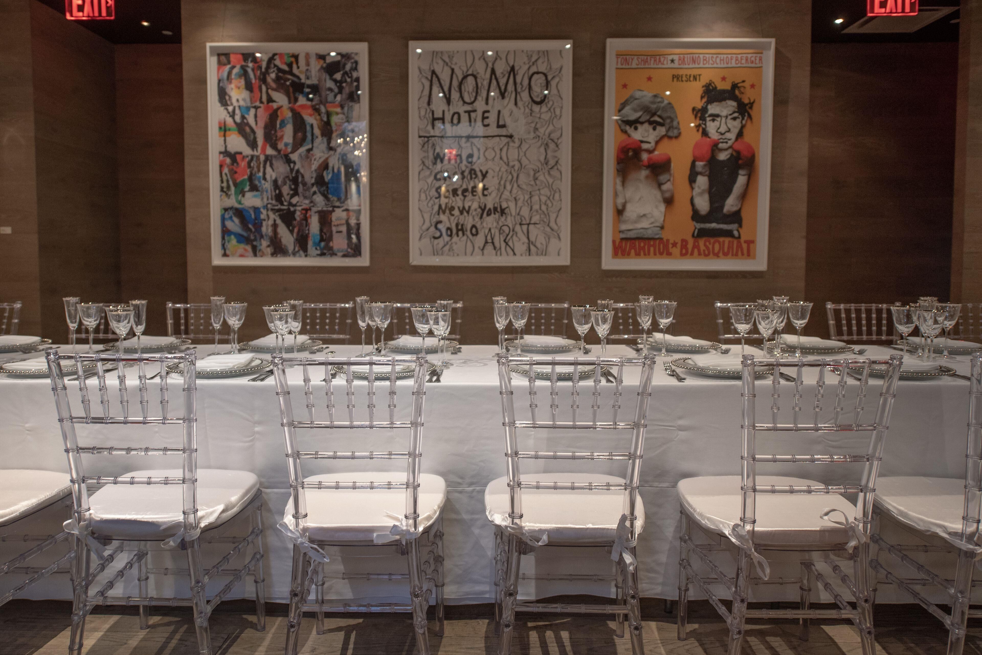 Un espace repas avec des chaises transparentes et des nappes blanches, agrémenté d’œuvres d’art exposées sur les murs.