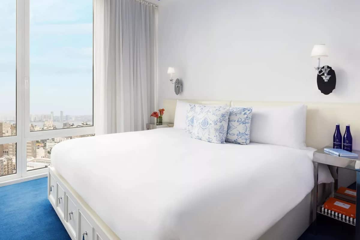 Une chambre d’hôtel avec un grand lit, une table de chevet avec une lampe, un vase de fleurs et une vue sur le paysage urbain.