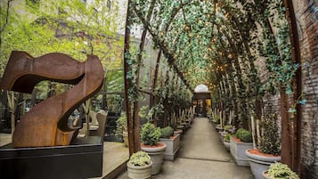 Un pasillo con una gran escultura metálica, plantas en macetas y una pared de ladrillo.