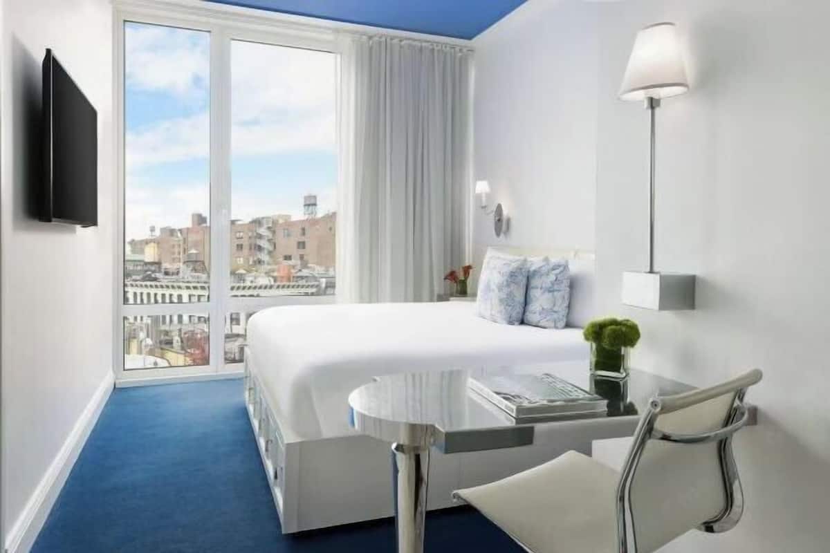 Une chambre d’hôtel avec un lit, un bureau, une chaise, une télévision, une lampe et une vue sur la ville.