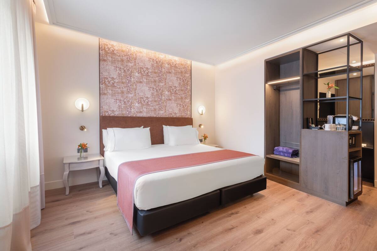 A modern hotel room with a large bed, a nightstand, a built-in wardrobe, and a decorative headboard.