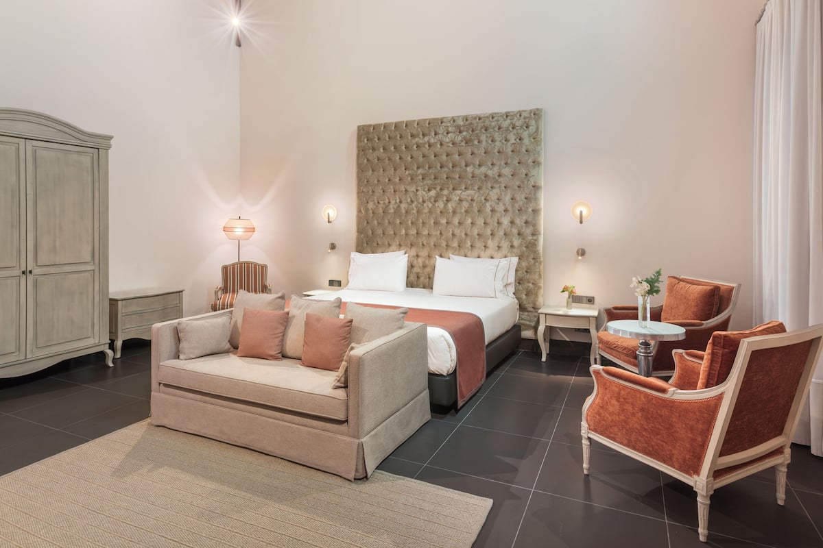 A hotel room with a bed, a sofa, a chair, a small table, and a cabinet.