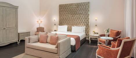 A hotel room with a bed, a sofa, a chair, a small table, and a cabinet.