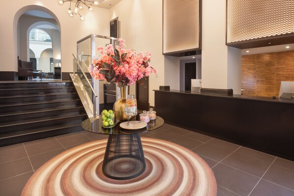 A reception area with a glass-top table, a vase with pink flowers, and a fruit bowl. - Eurostars Sevilla Boutique (Seville)