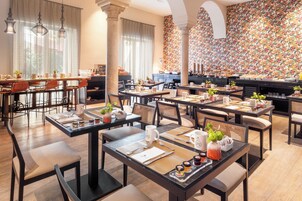 A hotel dining area with multiple tables set for breakfast, featuring a variety of breakfast items and condiments.