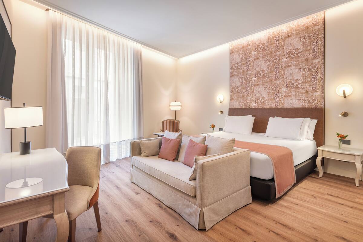 A hotel room with a bed, a sofa, a desk, and a nightstand.