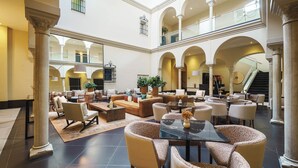 A spacious lobby with multiple seating areas, including sofas and chairs, a central coffee table, and a staircase leading to an upper level. - Eurostars Sevilla Boutique (Seville)