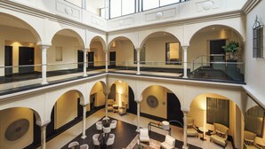 A spacious atrium with multiple levels, featuring a central seating area with sofas and chairs, surrounded by arches and a high ceiling with intricate woodwork. - Eurostars Sevilla Boutique (Seville)