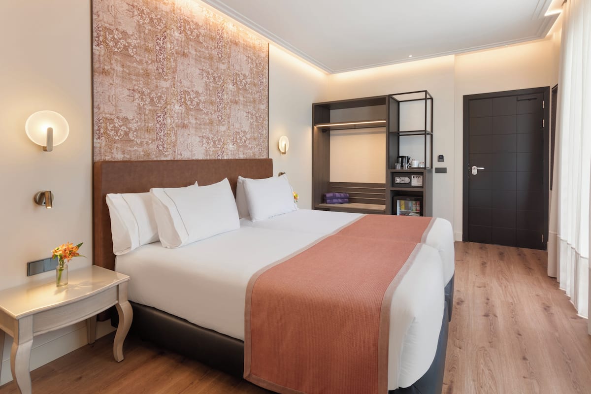 A modern hotel room with a large bed, bedside tables, a wardrobe, and a bathroom door.
