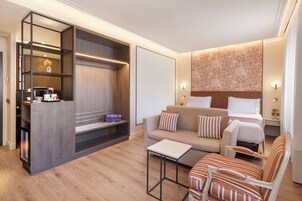 A modern hotel room with a sofa, a chair, a coffee table, a TV, and a wardrobe.