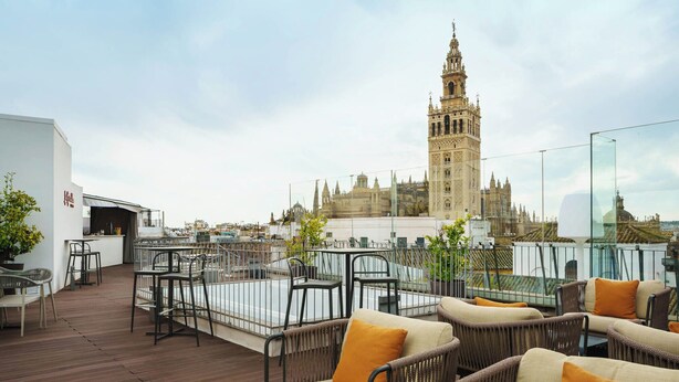 A rooftop terrace with wicker furniture and a view of a historic building with a clock tower. - Eurostars Sevilla Boutique (Seville)