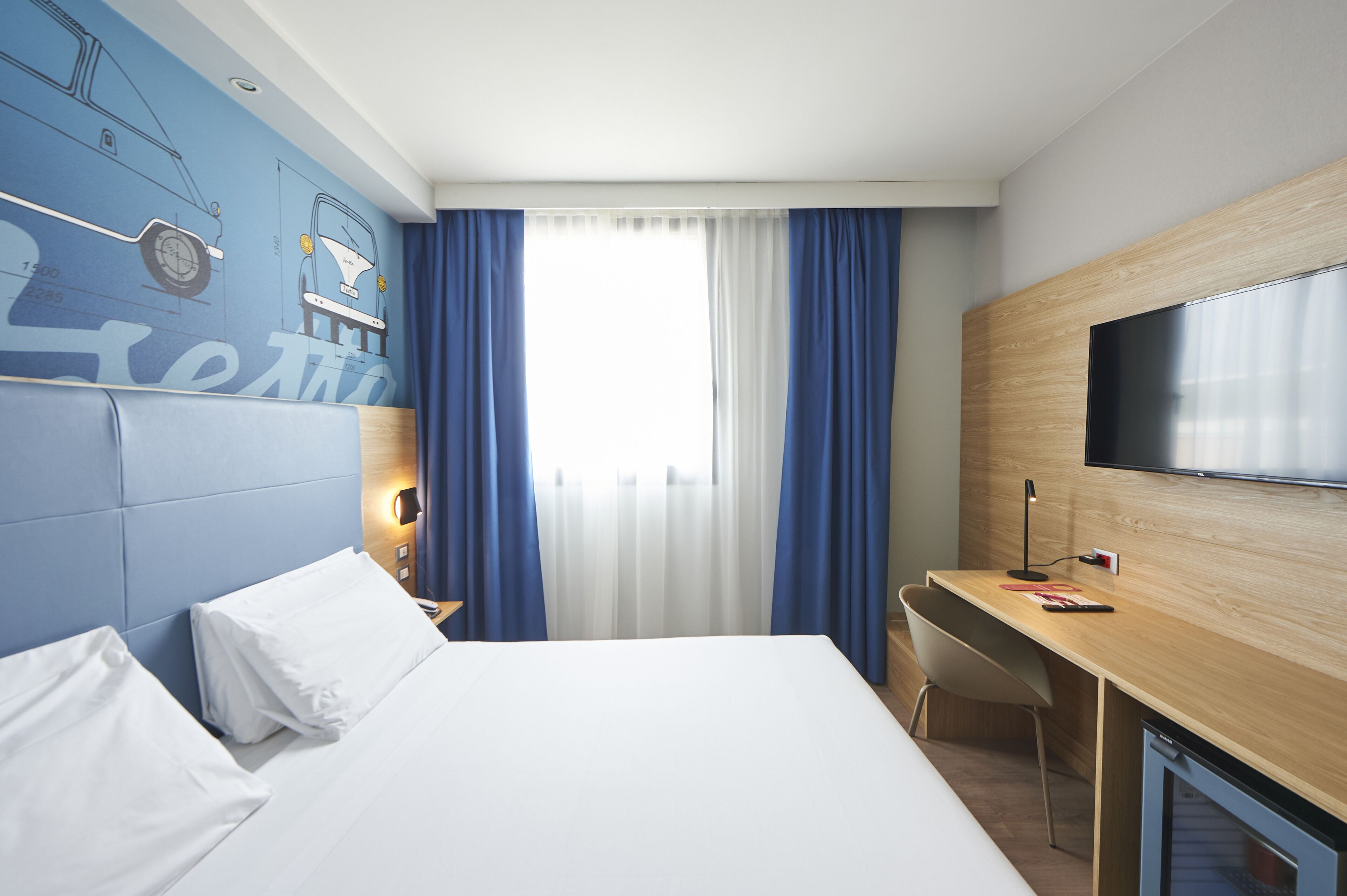 A hotel room with a bed, a desk, a TV, and a window with curtains.