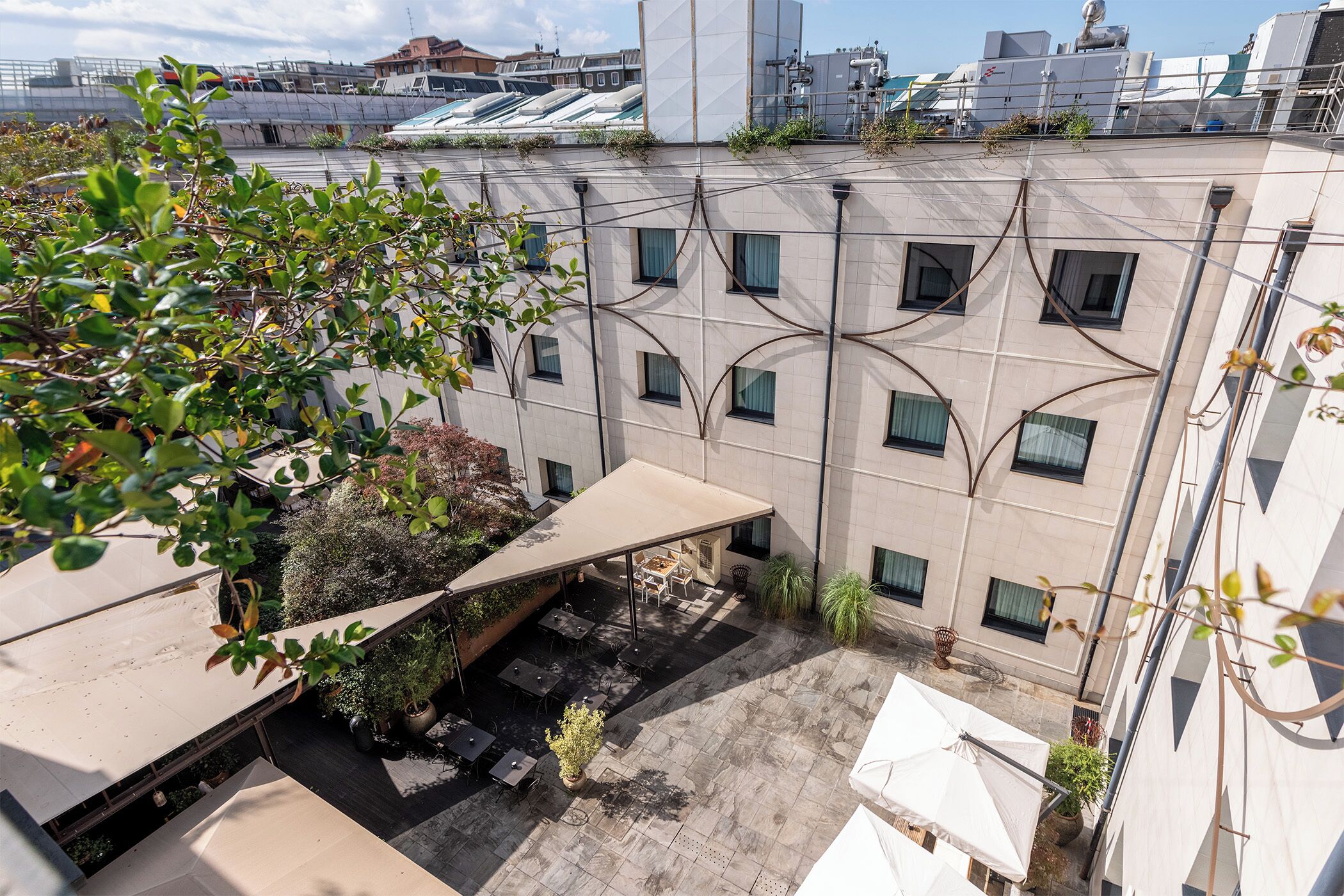 A rooftop terrace with outdoor seating, potted plants, and a view of adjacent buildings.