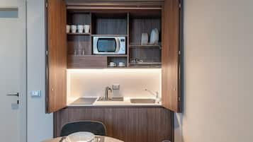 Una kitchenette compacta con microondas, lavamanos y estantes de almacenamiento.