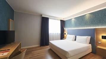 Ein modernes Hotelzimmer mit einem großen Bett, einem Schreibtisch mit Flachbildfernseher und einem Fenster mit Vorhängen.