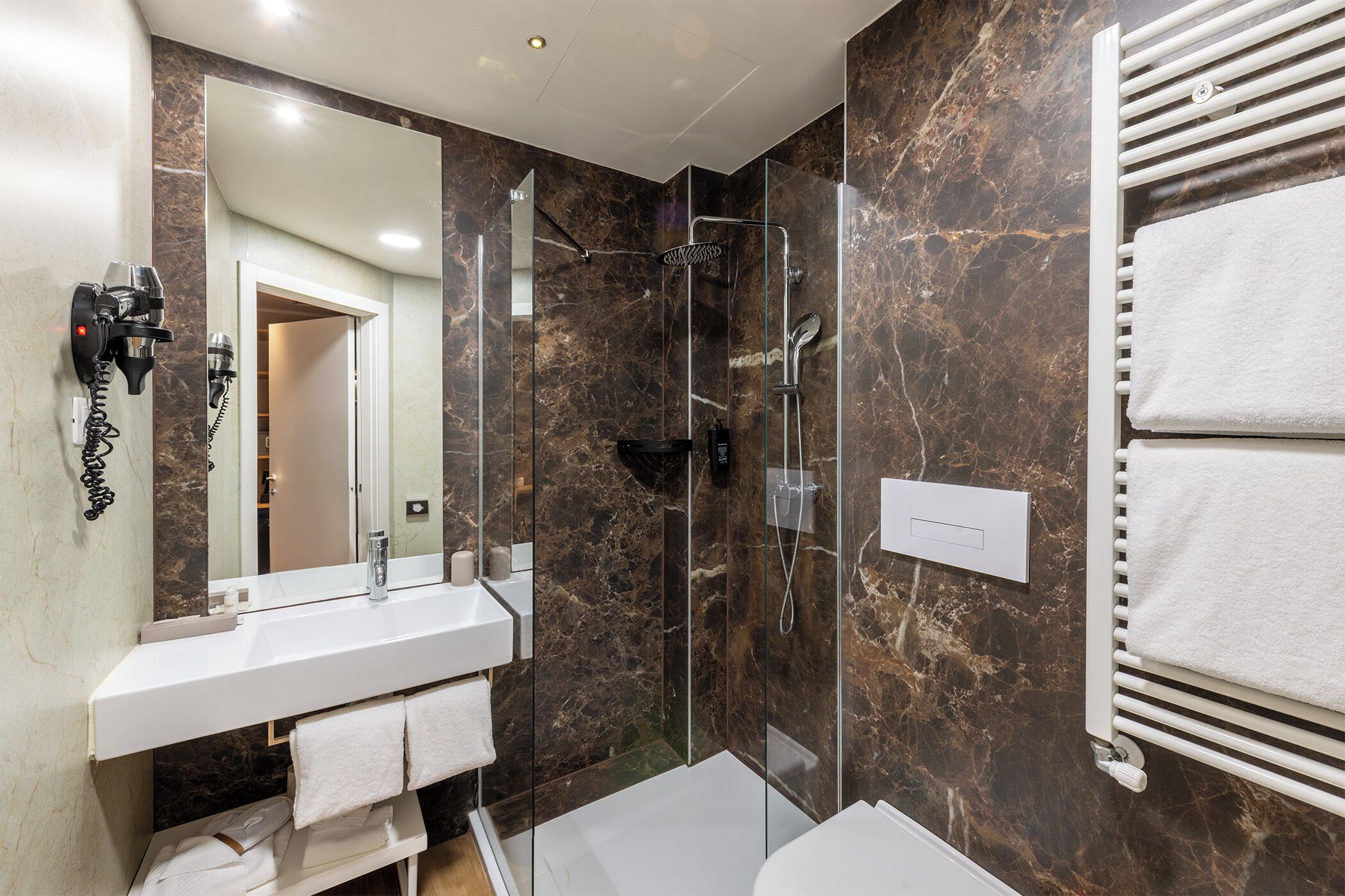Un baño moderno con ducha acristalada, un lavabo blanco y un perchero para toallas.