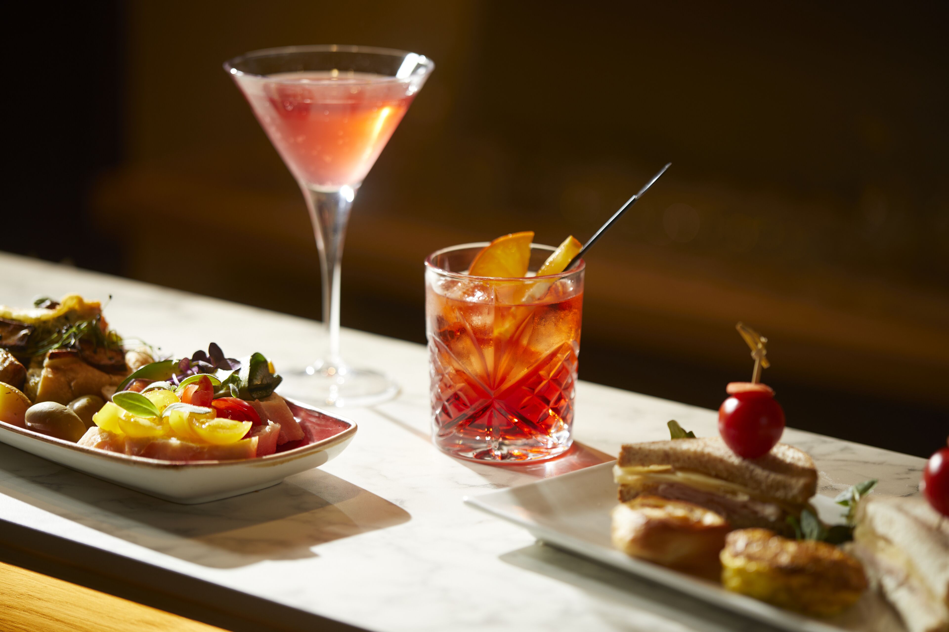 A table with a martini glass and a cocktail with fruit garnish.