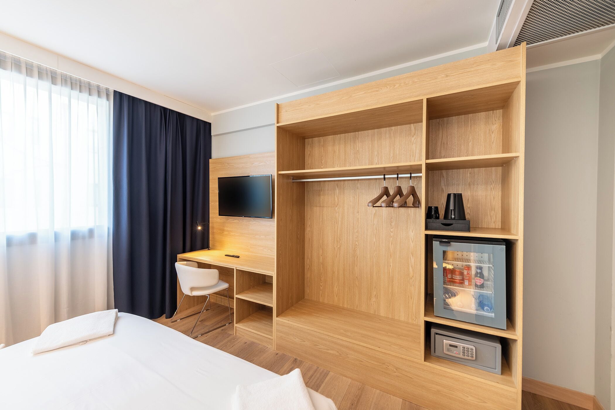 Ein Hotelzimmer mit Bett, Schreibtisch, Fernseher, Kleiderschrank und Minikühlschrank.