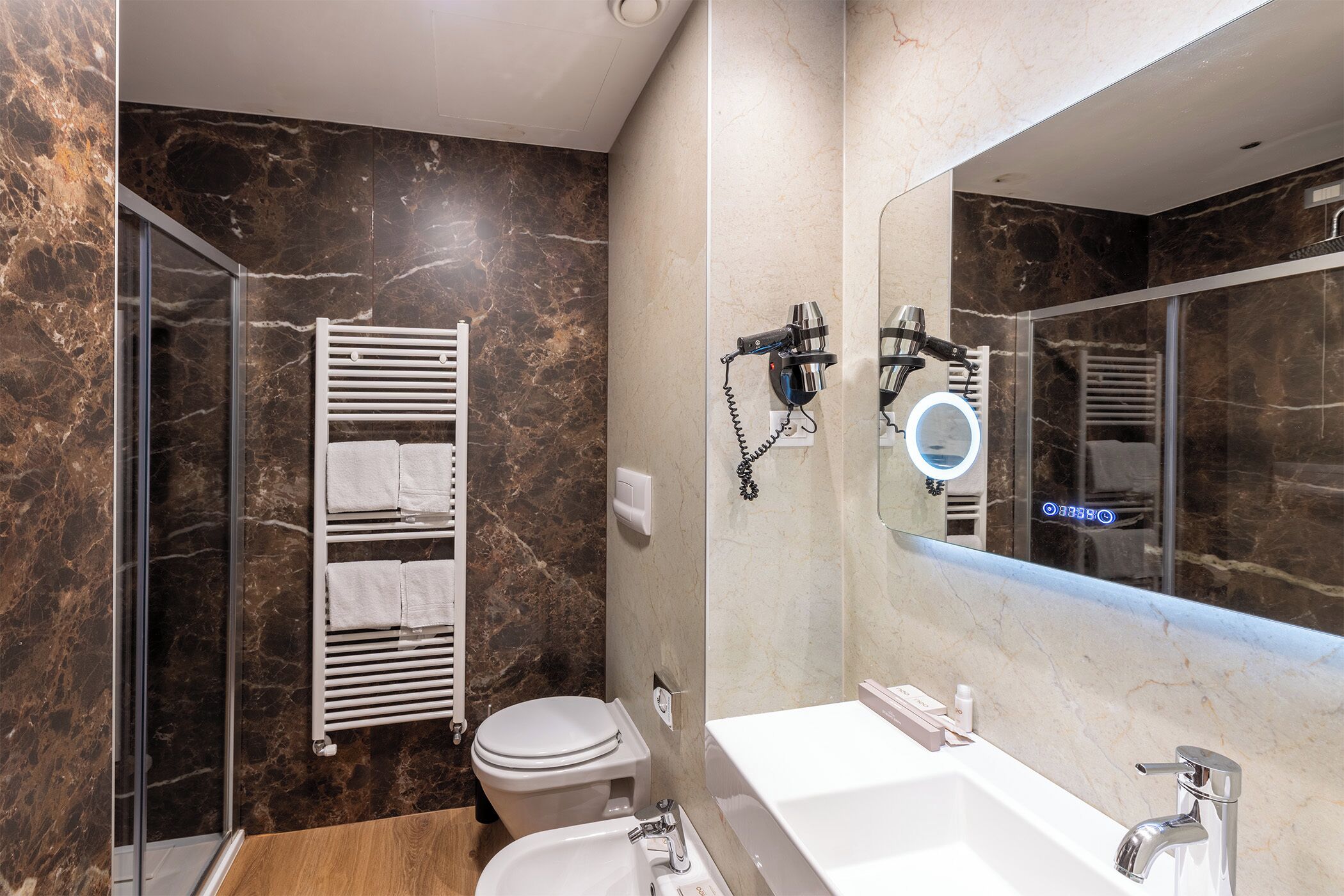 Un baño moderno con cabina de ducha de vidrio, inodoro y lavamanos blancos, y un espejo grande.