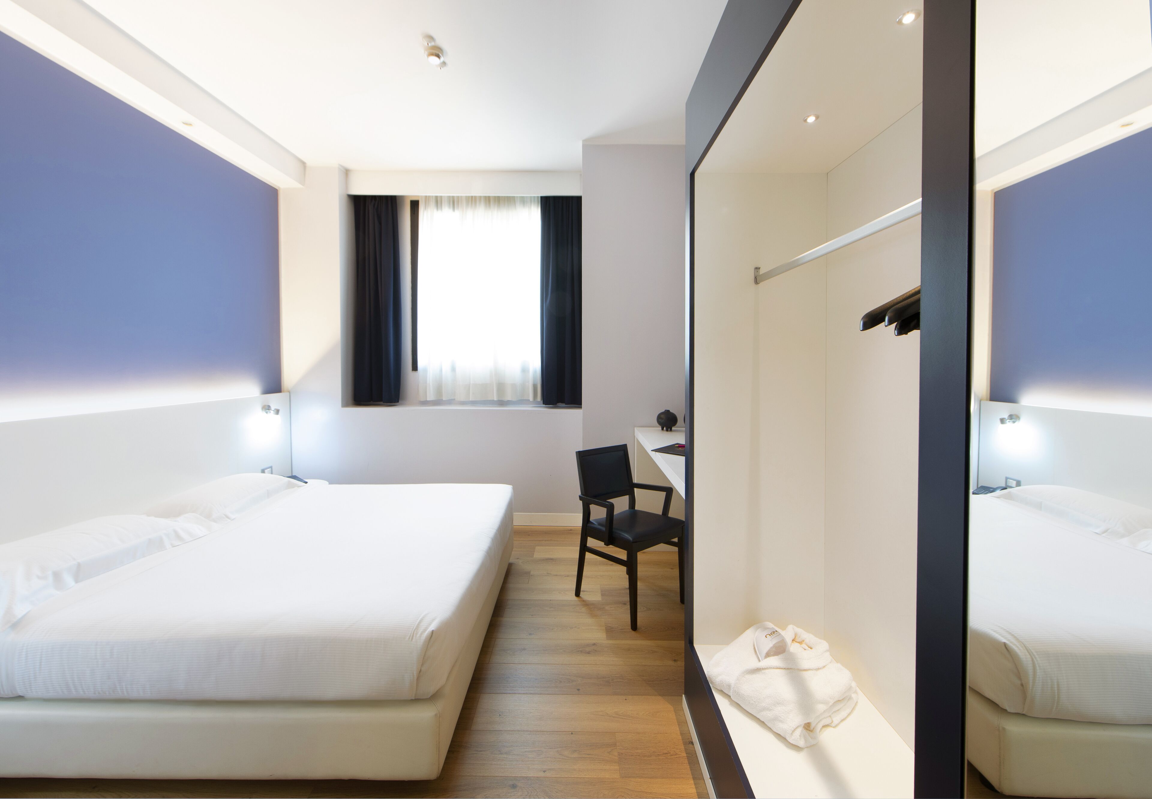Habitación de hotel con dos camas, un escritorio, una silla y una ventana con cortinas.