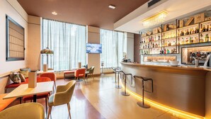 Una zona de bar moderna con una barra larga, estantes llenos de botellas de licor y una pantalla de televisión.