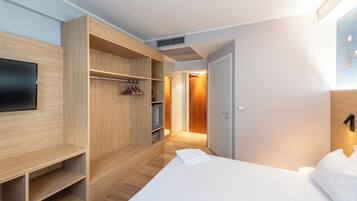 Ein modernes Hotelzimmer mit einem Holzschrank, einem Bett und einem Fernseher.