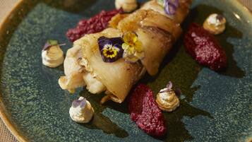 A plate with a dish of food, garnished with flowers and small dollops of cream.