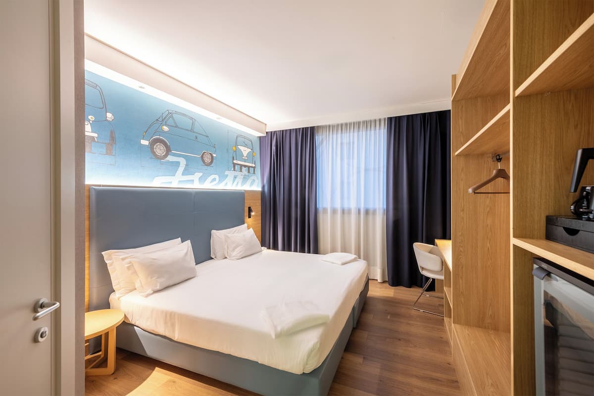 Moderni hotellihuone, jossa on siististi pedattu sänky, työpöytä ja vaatekaappi.