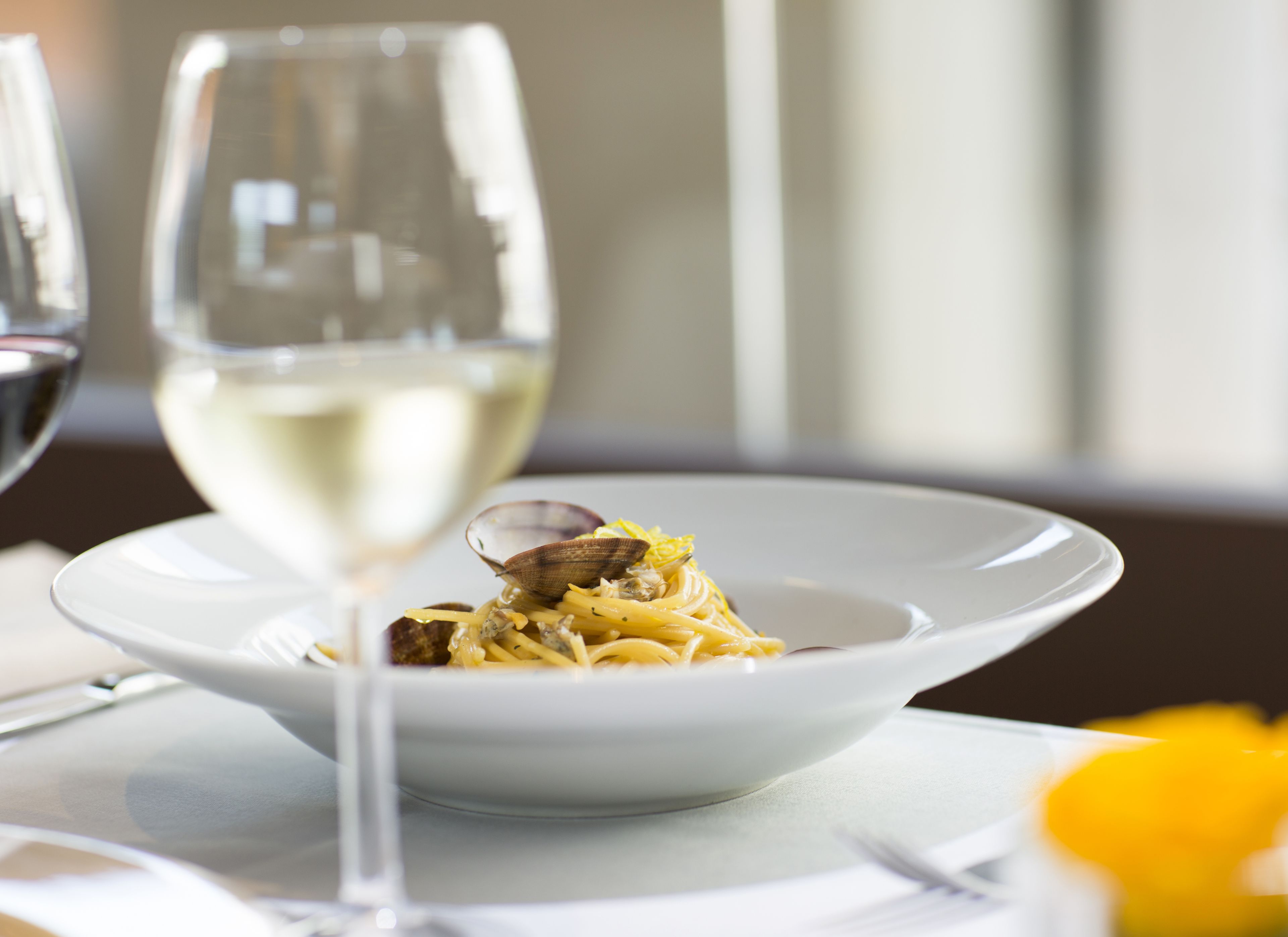 A plate of pasta with clams and a glass of white wine on a table.