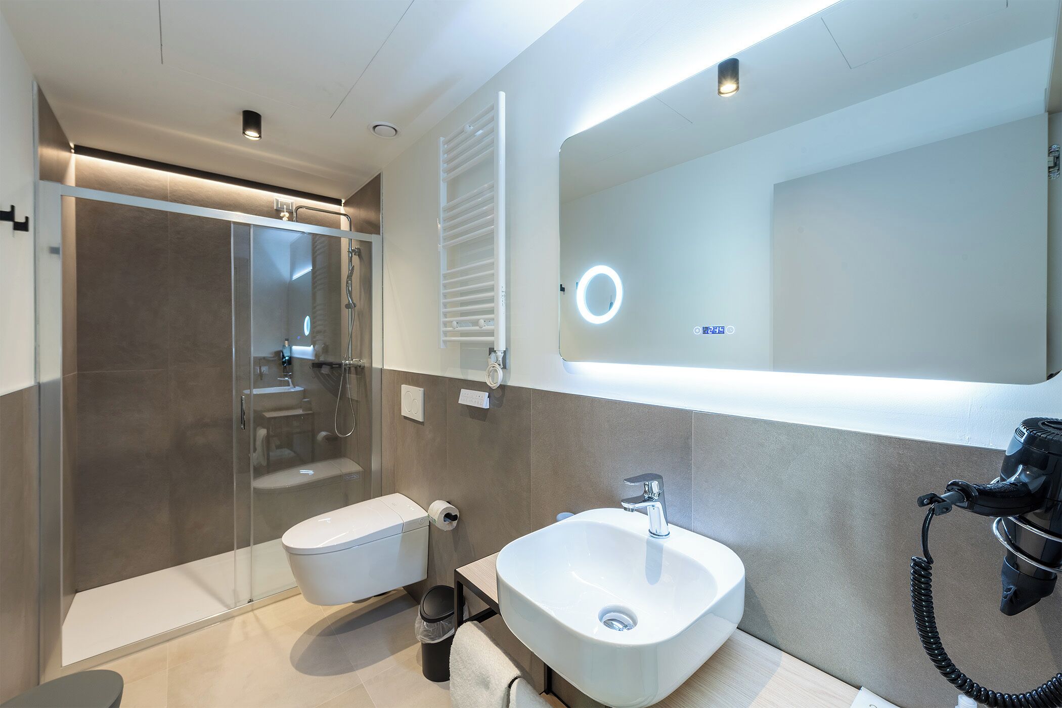 Un bagno moderno con cabina doccia in vetro, un lavandino bianco e un ampio specchio con luce ad anello.
