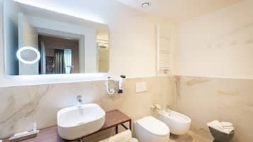 A modern bathroom with a large mirror, two sinks, a bidet, and a towel rack.