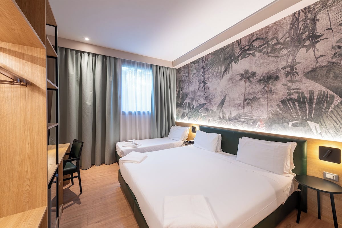 Hotellihuone, jossa on suuri sänky, kaksi yöpöytää, työpöytä tuolilla sekä suuri seinämaalaus.