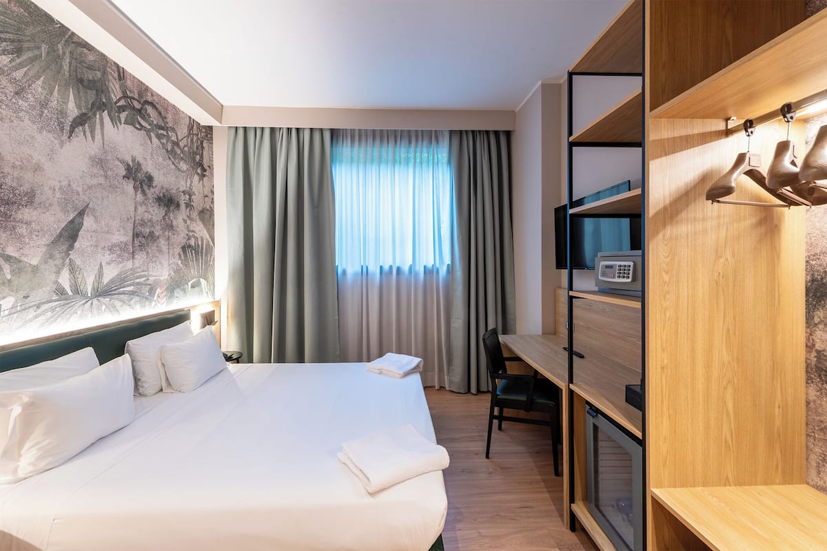 Hotellihuone, jossa on sänky, työpöytä, televisio ja vaatekaappi.