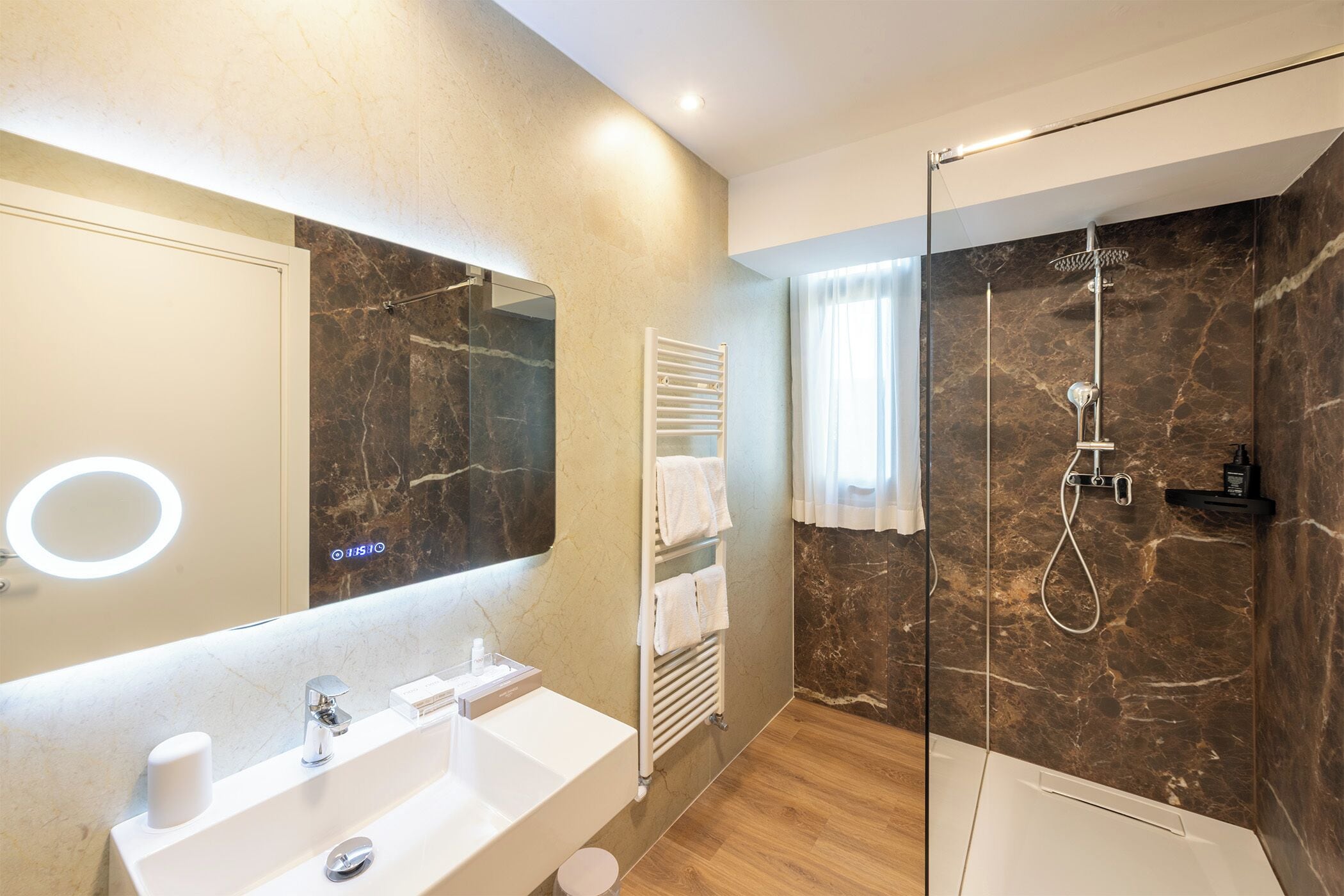 A modern bathroom with a marble wall, a glass-enclosed shower, a white sink, and a towel rack.